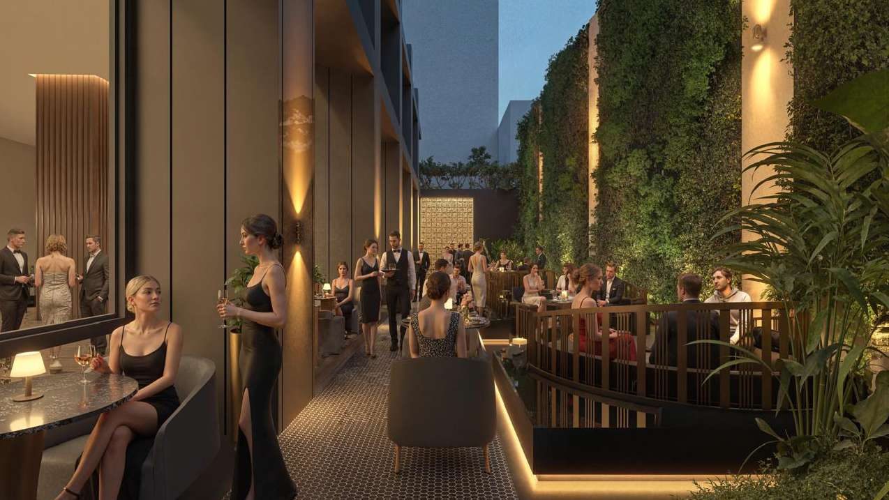 Terraza jardín iluminada al anochecer, con muros verdes y huéspedes conversando